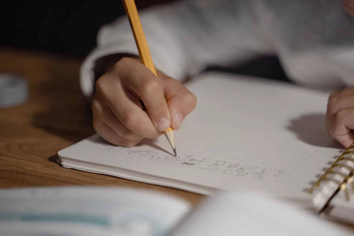 A child's hand writing on a worksheet with a pencil
