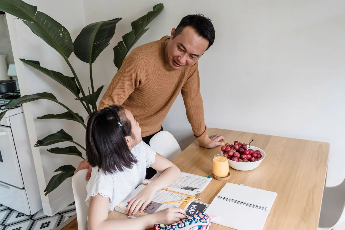A parent helping a child with homework at the kitchen table